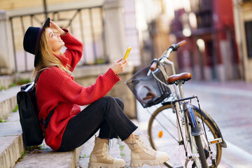 Woman with mobile phone looking up while sitting by bicycle on steps