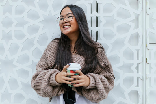 Smiling young woman holding coffee cup while standing against metal gate