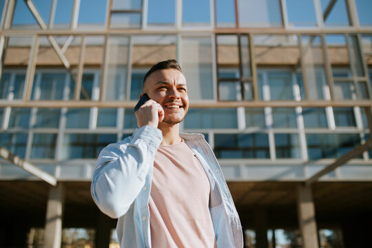 Mid adult man smiling while talking on mobile phone standing against building