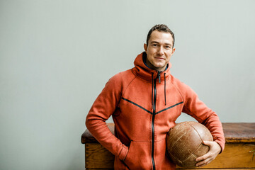 Male athlete with hands in pockets holding medicine ball against wall
