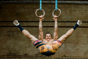 Excited male athlete with leg split hanging through gymnastic rings at health club