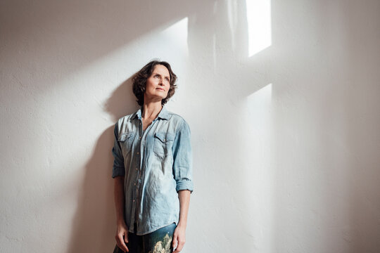 Thoughtful woman standing in front of white wall