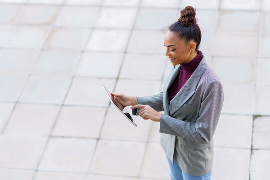 Smiling businesswoman using digital tablet while standing on footpath