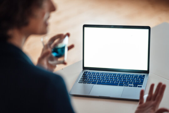 Woman holding glass while gesturing sitting in front of laptop screen
