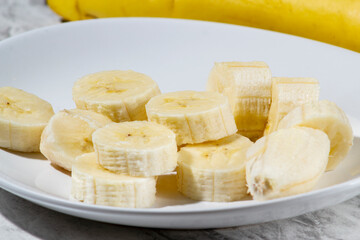 A bunch of bananas and a sliced banana on a plate on a table