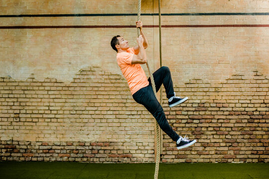 Man climbing on rope by brick wall at gym
