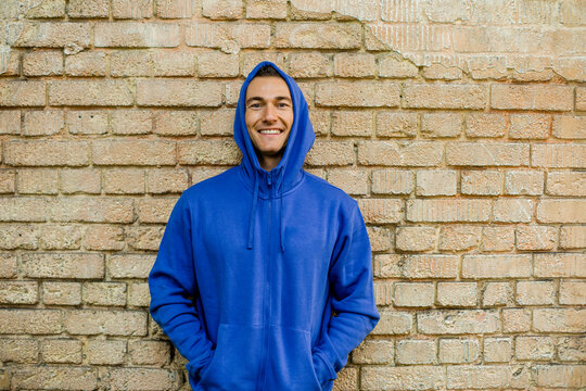Smiling male athlete in blue jacket against brick wall
