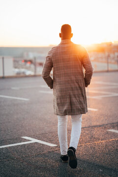 Man with hands in pockets walking at parking lot during sunset