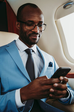 Smiling businessman text messaging on smart phone while traveling through airplane