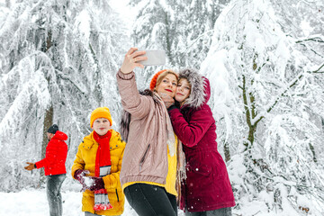 Mother and daughter taking selfie through mobile phone while standing with family in background at forest