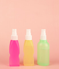 Three trendy colorful small 100ml sprayer bottles plastic hand sanitizer alcohol disinfectant spray or shampoo cream on pink background