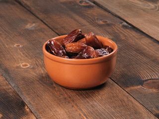 Dates in a brown ceramic bowl on a wooden background