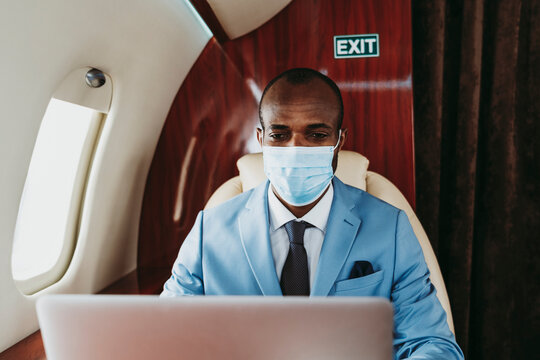 Young businessman working on laptop in airplane during pandemic