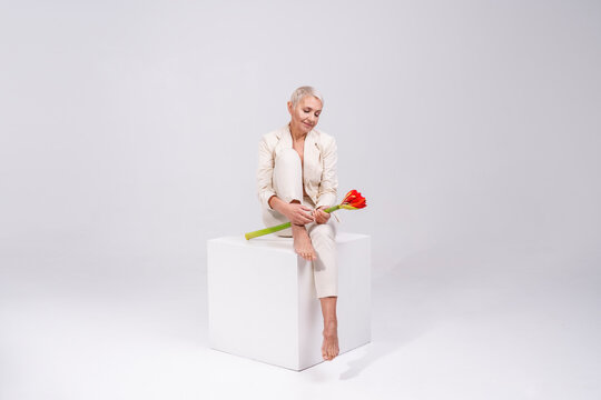 Senior woman holding flower while sitting against gray background