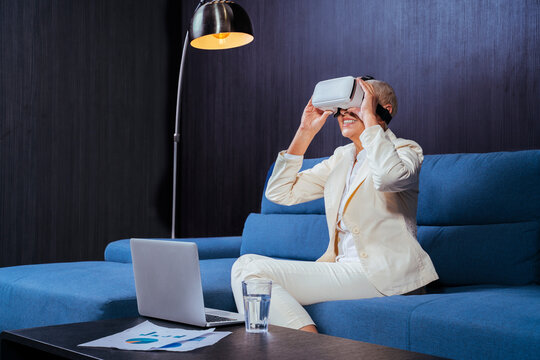 Smiling businesswoman using virtual reality headset while sitting by laptop on sofa