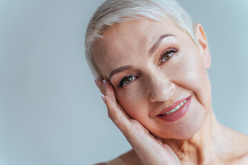 Senior woman smiling while standing against gray background