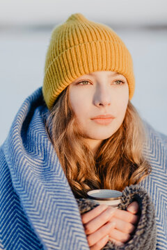 Portrait of beautiful teenage girl wearing knit hat warming herself up with wool blanket and mug of hot tea