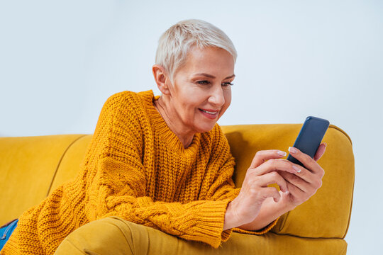 Smiling senior woman using mobile phone while relaxing on sofa