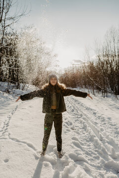 Portrait of teenage girl standing in snow with raised arms and closed eyes