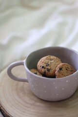 Bowl of chocolate chip cookies and wooden tray on a bed. Selective focus.