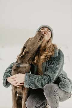 Portrait of teenage girl crouching in snow and embracing Labrador Retriever