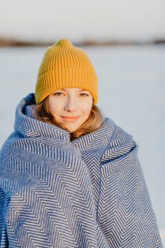 Portrait of beautiful teenage girl wearing knit hat warming herself up with wool blanket