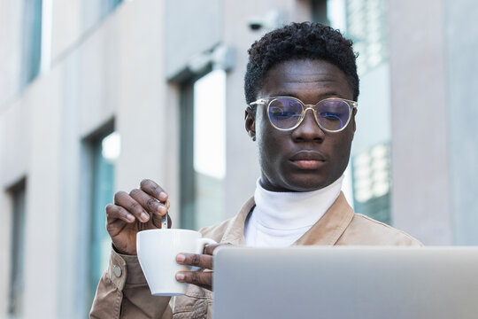 Young man stirring coffee while looking at laptop at sidewalk cafe