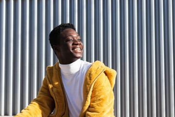 Smiling African man in yellow jacket against white wall looking away 