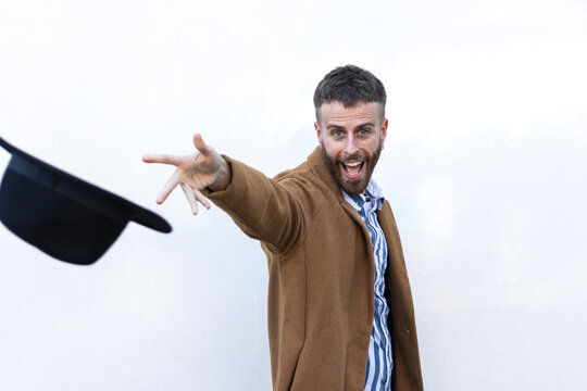 Happy businessman throwing hat while standing against white wall