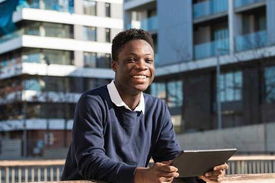 Smiling young man with digital tablet leaning on railing against building during sunny day