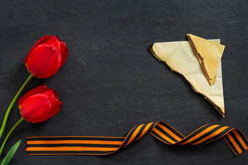 May 9 Russian Victory Day. St. George ribbon with stack of letters and bouquet of red tulips on  black granite monument with empty space for text.