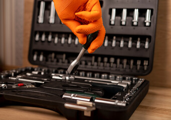 Male hand in building glove with socket ratchet handle, taken from toolbox. Industrial metal tool,...