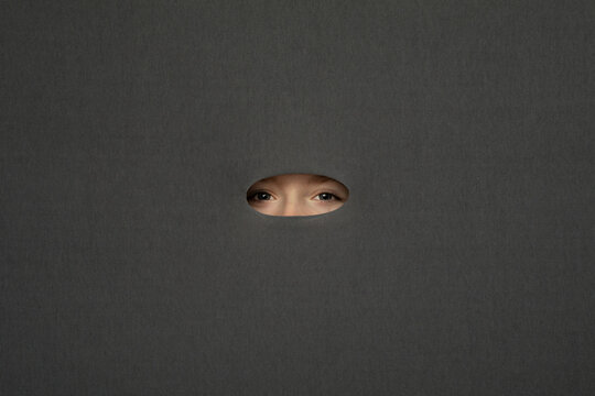 Eyes of teenage girl peeking through hole in gray background
