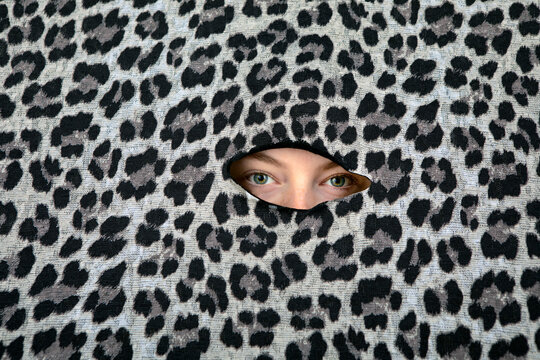 Eyes of teenage girl peeking through hole in leopard print pattern