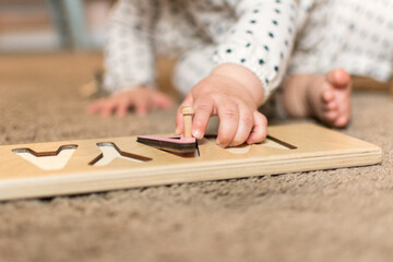 Toddler reaches for puzzle piece in letter name puzzle; pincer grasp on wooden peg