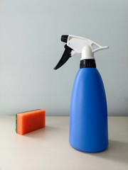 Cleaning and disinfecting the premises. Orange sponge and blue sprayer on a table against a light wall