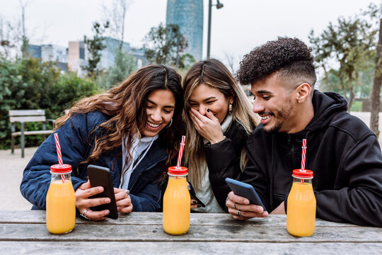 Cheerful female friends with young man using smart phone
