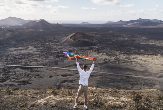 Young male tourist waving rainbow flay while standing at El Cuervo Volcano during vacations, Lanzarote, Spain