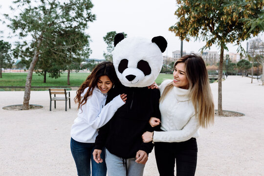 Happy Female Friends Having Fun With Male Friend Wearing Panda Mask At Park