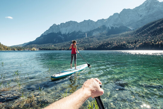 Germany, Bavaria, Garmisch Partenkirchen, Young couple stand up padling on Lake Eibsee, overlooking Zugspitze Mountain