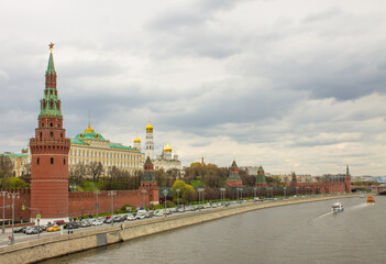 Moscow / Russia - May, 5, 2021: view of the brick wall, the yellow Grand Kremlin Palace and the Assumption Cathedral with golden domes on the banks of the Moskva River on a cloudy spring day