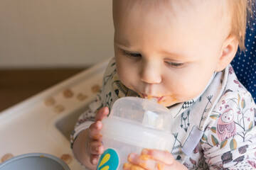 Young toddler learning to use a straw cup to drink water; promoting lip closure, cheek tightening, and tongue elevation