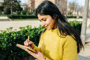 Smiling woman writing in diary in public park