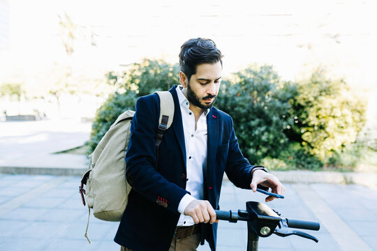 Mid adult businessman with backpack using mobile phone while standing by bicycle