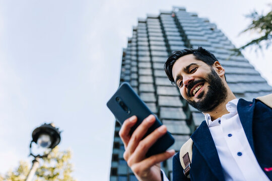 Smiling businessman using smart phone while standing in city