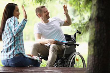 Joyful woman and man in wheelchair holding hands in park in greeting