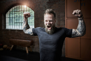 Male athlete screaming while flexing muscles in gym