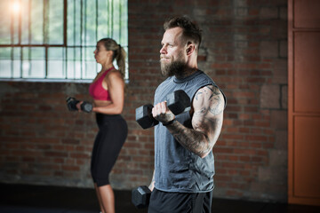 Active female and male athlete exercising with dumbbells in gym