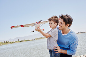 Boy holding airplane toy while standing by father on sunny day