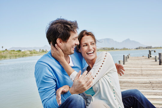 Laughing couple with arms around sitting on pier